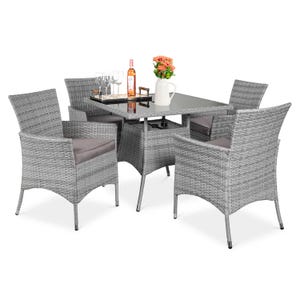 A gray wicker outdoor dining set includes a glass-top table and four cushioned chairs. On the table are wine glasses, a bottle of wine, and a vase with flowers.