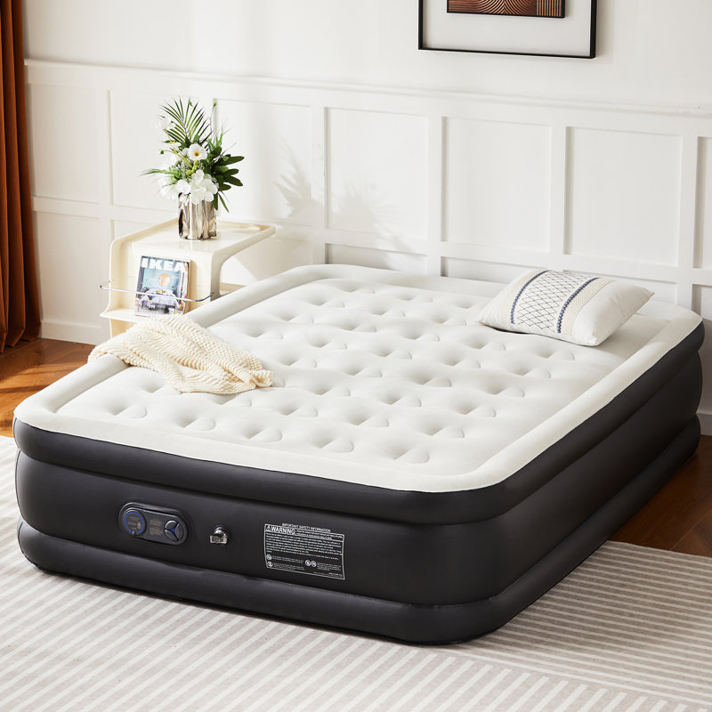 Queen 18\“ air mattress with a built-in pump, featuring a tufted, soft-top design. A pillow and blanket are on the mattress, placed in a room with white-panel walls.