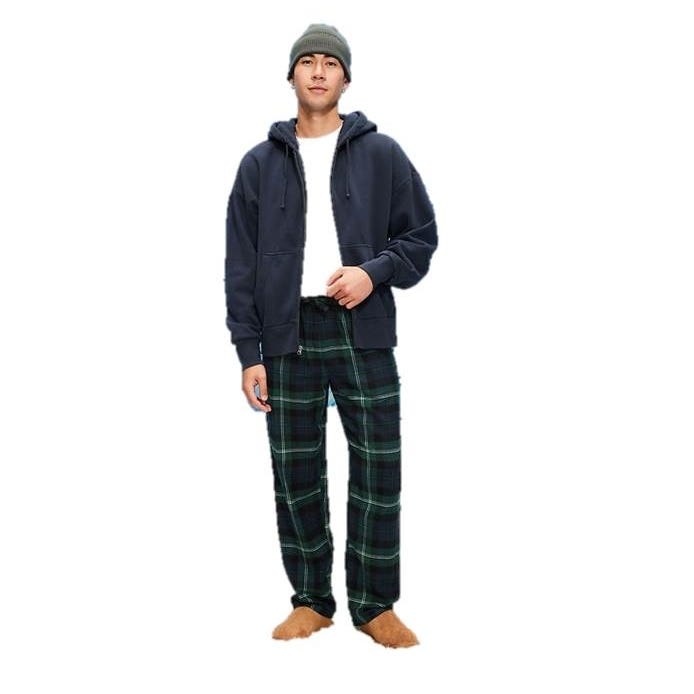 A person is wearing a navy hoodie, white shirt, green plaid pajama pants, and brown fuzzy slippers, along with a green knit beanie.