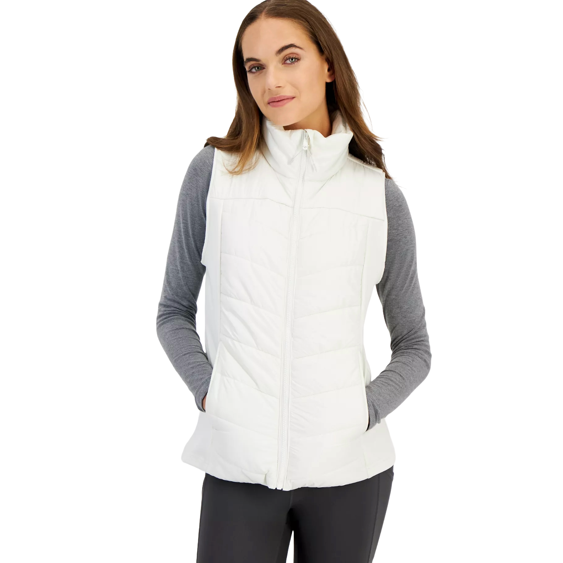 A woman is wearing a white quilted vest over a gray long-sleeve shirt with black pants.