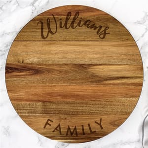 Round wooden cutting board with engraved text \“Williams Family,\“ suitable for personalized kitchen decor.
