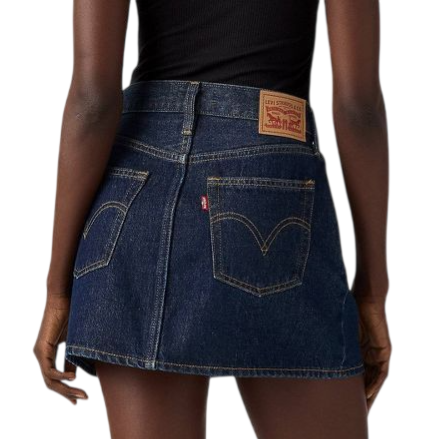 A person is wearing a dark denim mini skirt with two back pockets and a leather patch, paired with a black top and black shoes with low heels.