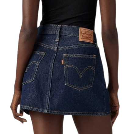 A person is wearing a dark denim mini skirt with two back pockets and a leather patch, paired with a black top and black shoes with low heels.