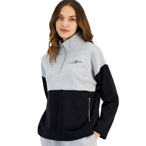 A woman wearing a grey, white, and black quarter-zip sweatshirt with a funnel neck and a logo on the left chest.