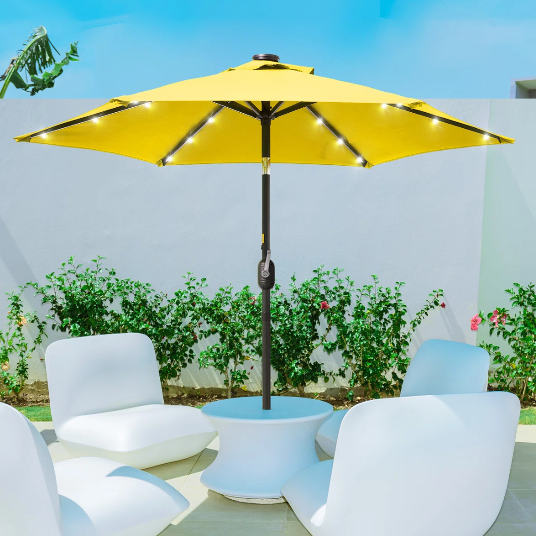 A yellow patio umbrella with built-in LED lights is paired with four modern white chairs arranged around a round table in an outdoor setting.