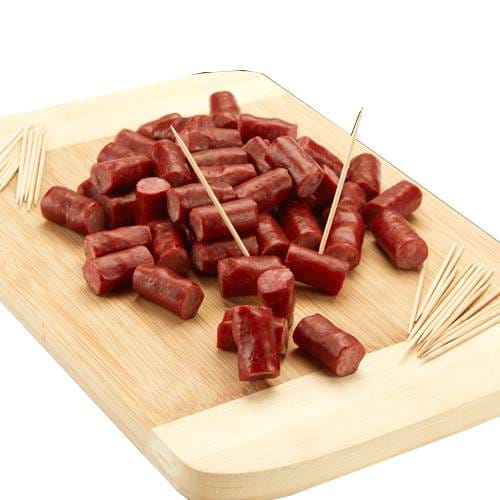 Small pieces of sliced sausage are arranged on a wooden cutting board, accompanied by toothpicks.