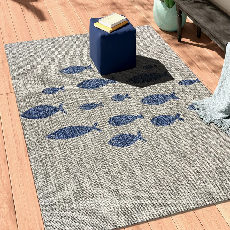 Grey outdoor area rug with a pattern of blue fish, accompanied by a small blue side table and a grey blanket.