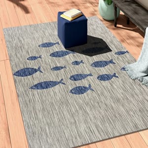 Grey outdoor area rug with a pattern of blue fish, accompanied by a small blue side table and a grey blanket.