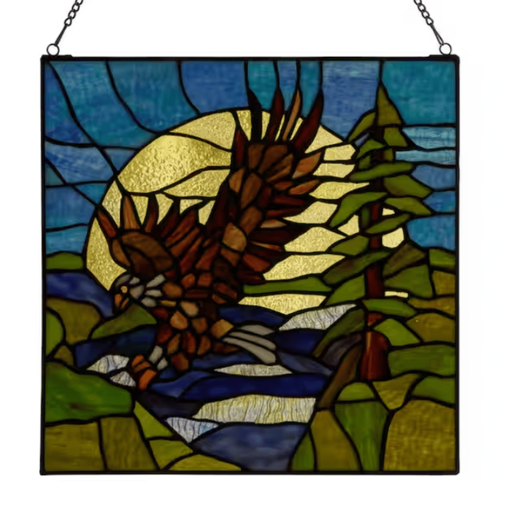 Stained glass panel featuring an eagle flying over a river with a tree and a sun in the background, set in a metal frame with a hanging chain.