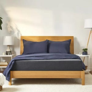 A neatly made bed with a wooden frame and dark blue bedding, accompanied by a white lamp and small plants on side tables.