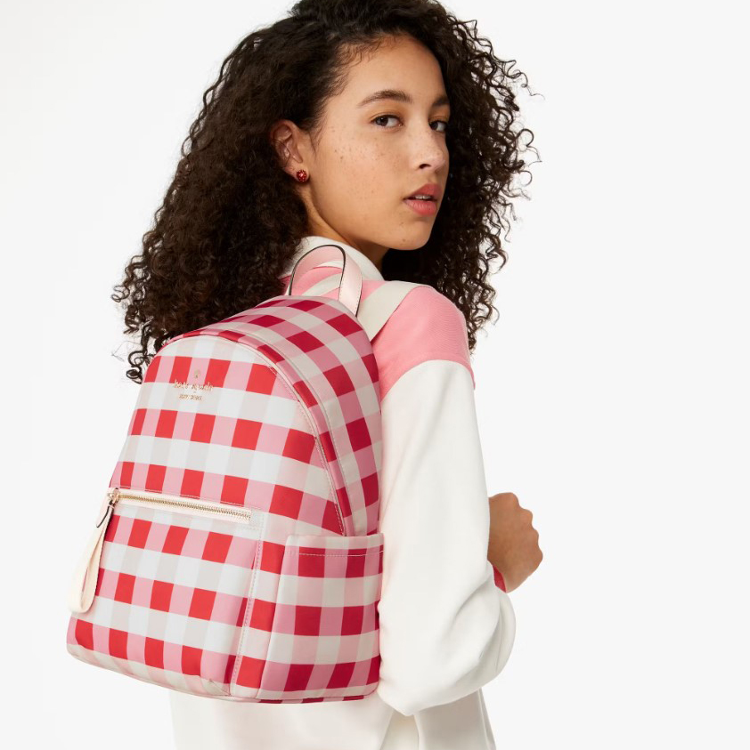 A medium-sized backpack with a pink and white checkered pattern, featuring a front zip pocket and adjustable straps.