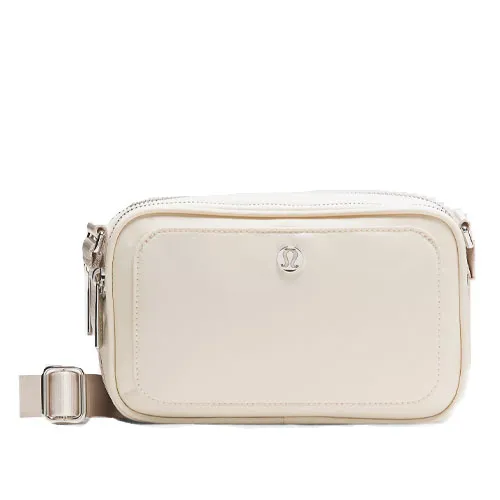 A small white crossbody bag with an adjustable strap, featuring a central logo and a front pocket with a zipper.