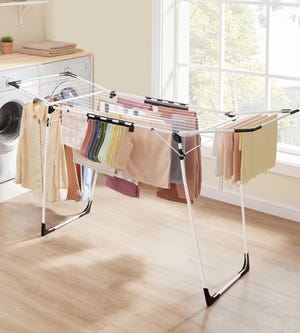 A clothes drying rack with towels and garments hanging on it, set in a laundry room with a window.
