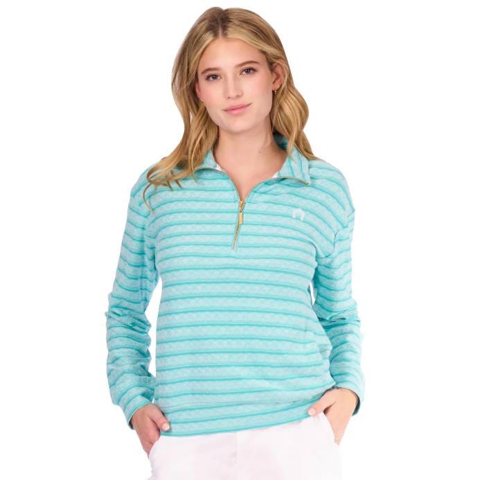 A woman wearing a light blue and white striped quarter-zip pullover with a small logo on the left chest, paired with white pants.