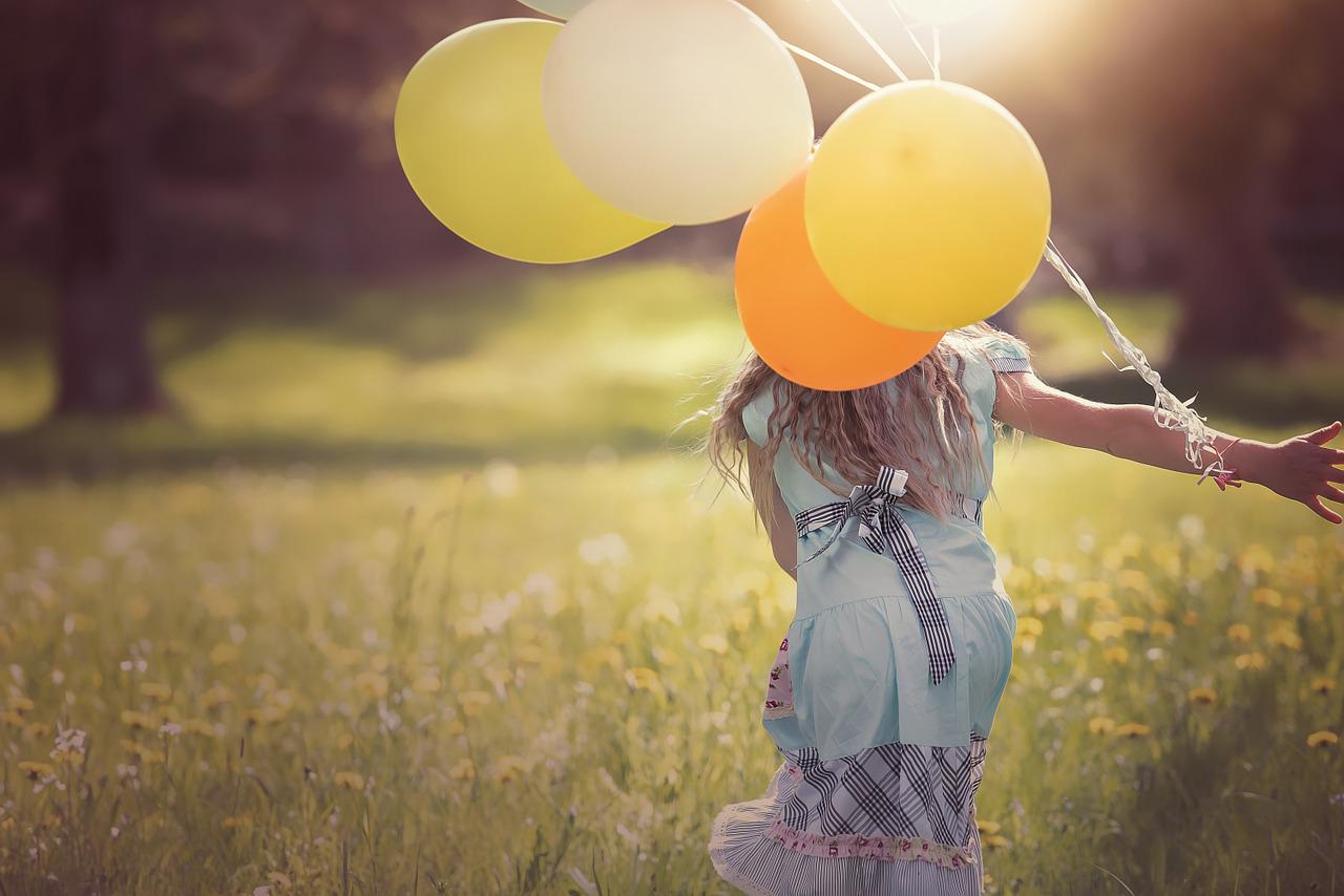 A person runs through a field with yellow and orange balloons