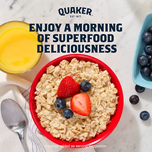 A bowl of oatmeal with fresh strawberries and blueberries on top, accompanied by a carton of blueberries and a glass of orange juice.