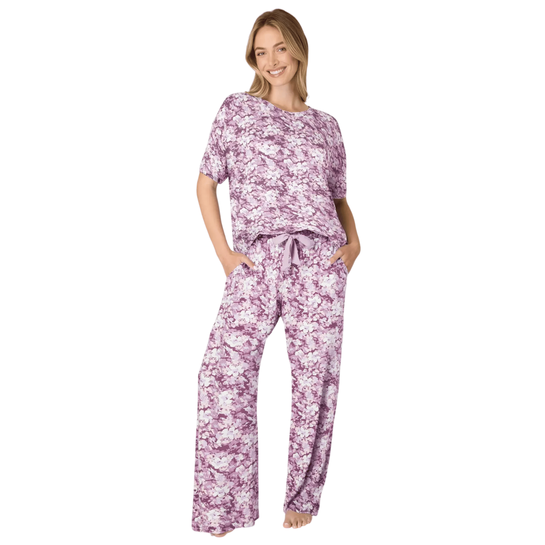 A woman wearing a purple and white floral pajama set, consisting of a loose-fitting short-sleeve top and wide-leg pants.