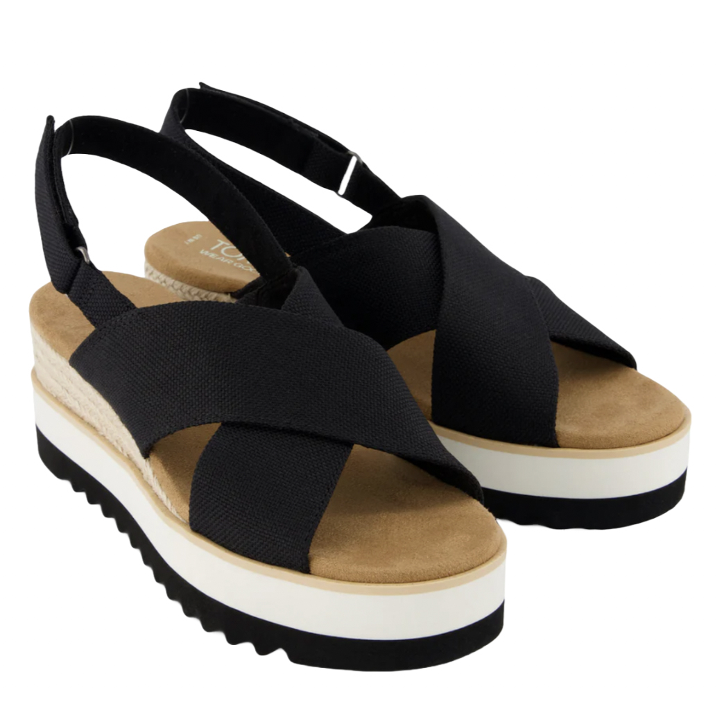 Black crossover wedge sandals with a comfortable tan footbed and adjustable slingback straps. They feature a platform sole with a white and black layered design.