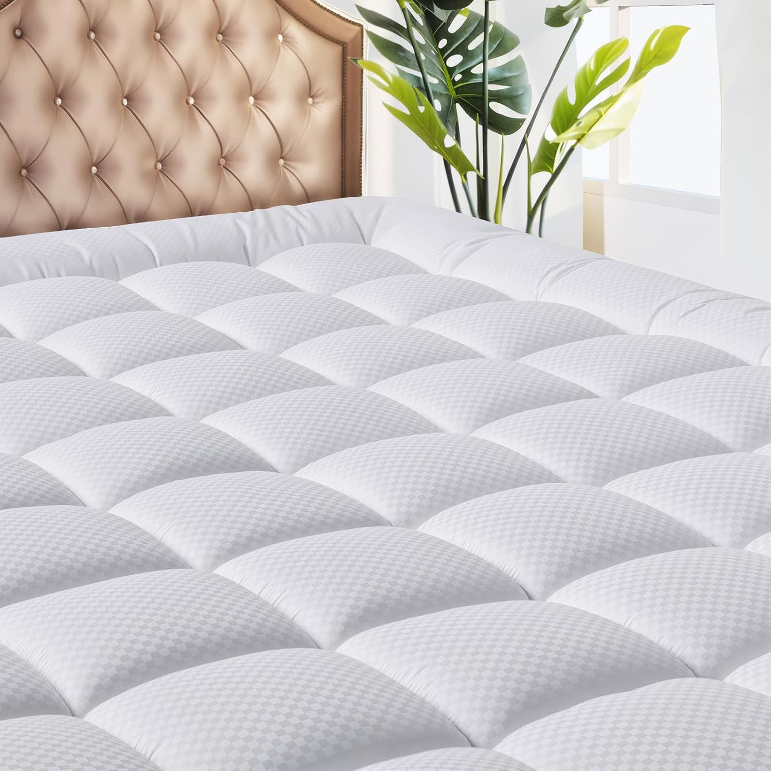 A white, quilted cooling deep-pocket mattress topper with a subtle checkered pattern, designed for comfort and breathability. It is shown on a bed with an elegant tufted headboard and accompanied by a potted plant.