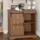 Wooden cabinet with a sliding barn door houses shelves on one side; coffee maker, jars, and a mug tree stand on top.