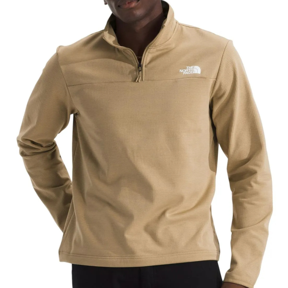 A beige quarter-zip pullover by The North Face, featuring a high collar and logo on the chest, worn by a person with hands on hips.