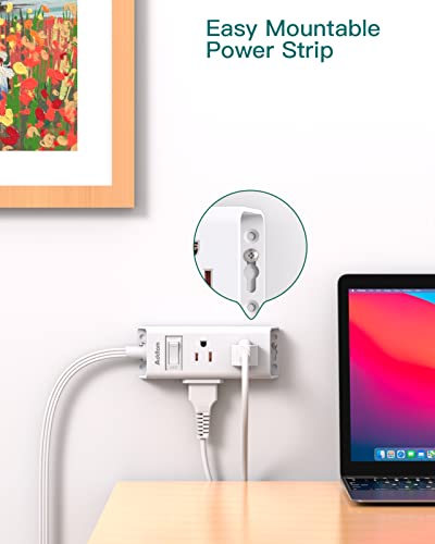 A power strip with a flat plug is mounted on the wall, with the cord running along the wall to a laptop on a desk.