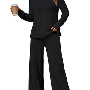 A woman is wearing a black, two-piece lounge set with long sleeves and wide-legged pants, paired with white sneakers. She is holding a coffee cup in her right hand.