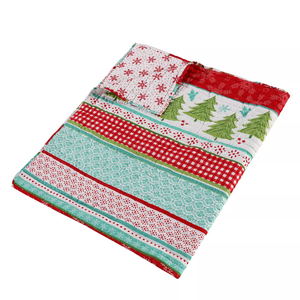 A Christmas-themed quilt with festive patterns including snowflakes, Christmas trees, and red and green stripes.