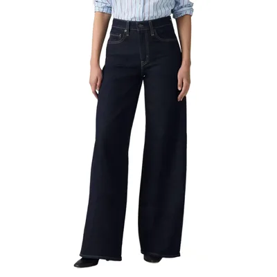 A person is wearing high-waisted, dark wash, wide-leg jeans paired with a light blue pinstriped shirt.