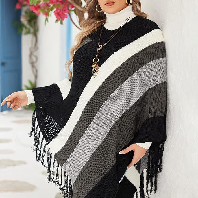 A woman is wearing a black, white, and gray striped poncho with fringe details and accessorized with a long necklace.