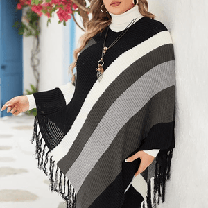 A woman is wearing a black, white, and gray striped poncho with fringe details and accessorized with a long necklace.