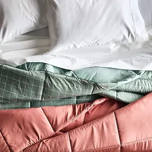 Two down-alternative comforters are shown, one in a solid mint green and the other in a peach color with a grid pattern.