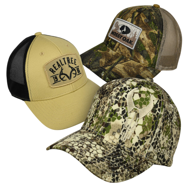 Three camouflage-themed baseball caps featuring brands: Realtree (tan with a black mesh back), Mossy Oak (multicolor camo), and a digital camo pattern cap with an unidentified logo.