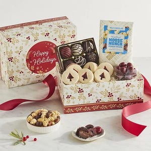 Holiday gift box with chocolate truffles, raspberry jam cookies, milk chocolate Moose Munch, and chocolate-covered cherries, alongside a bowl of mixed nuts.