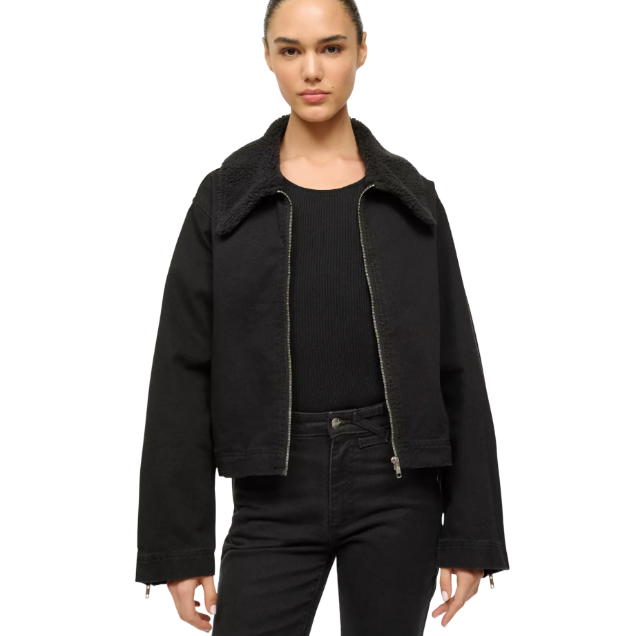 A person is wearing a black jacket with a sherpa collar over a black ribbed shirt and matching black pants.