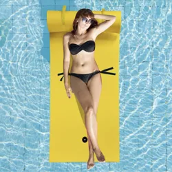 A person is lounging on a yellow floating mat in a swimming pool, wearing sunglasses and a black bikini.