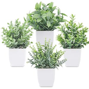 Three artificial potted plants with greenery in white square pots.