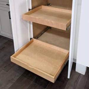 A wooden pull-out tray is installed in a cabinet with a clean, natural finish, featuring two tiers on smooth sliding rails, perfect for organizing kitchen or pantry items.