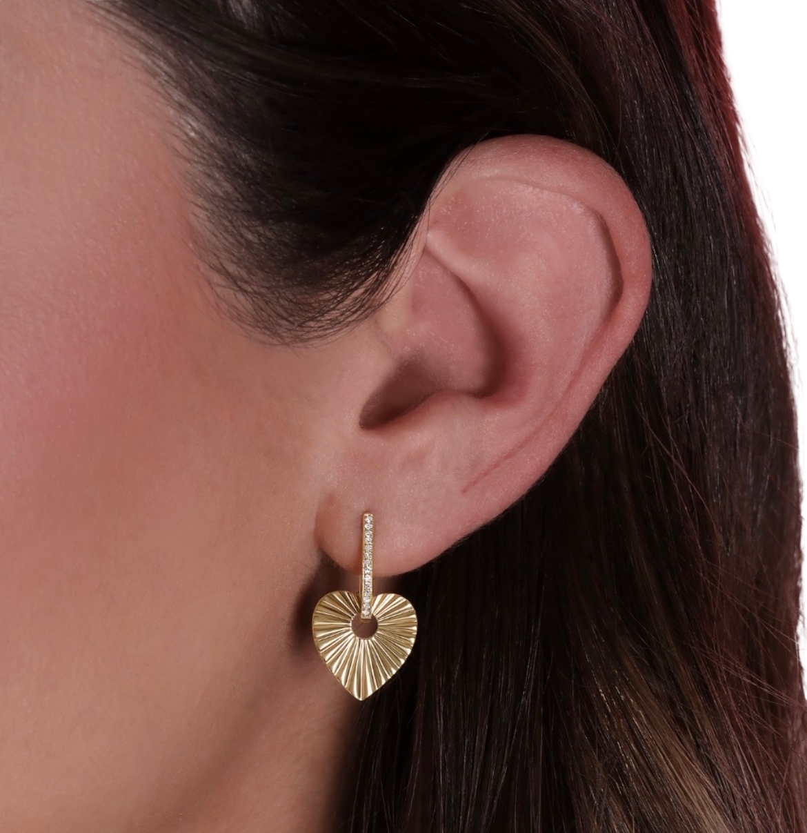 A person is wearing a gold heart-shaped earring with a ridged texture.