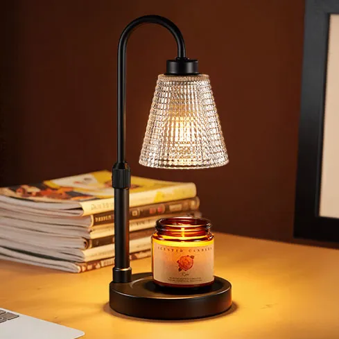 A black lamp with a textured glass shade illuminates a lit candle placed on its base. There are magazines stacked in the background.
