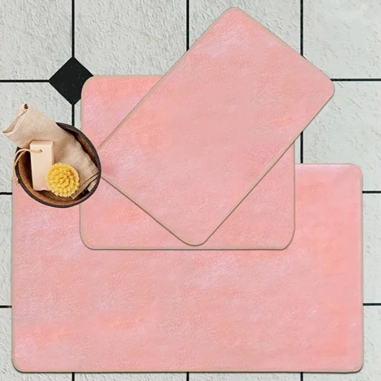 Three pink bath mats of varying sizes with a circular basket containing a beige towel and a yellow sponge.