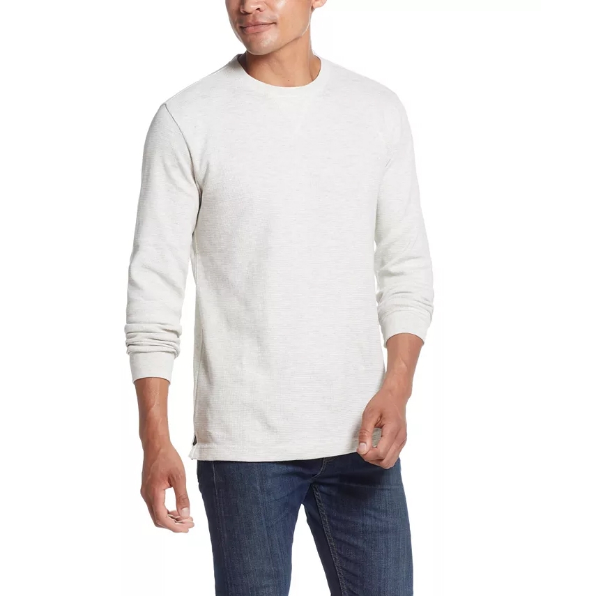 A man wearing a long-sleeved white crew neck shirt paired with dark blue jeans.
