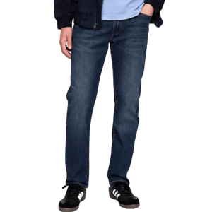 A person wearing dark blue jeans, a blue shirt, a black jacket, and black sneakers with white stripes.