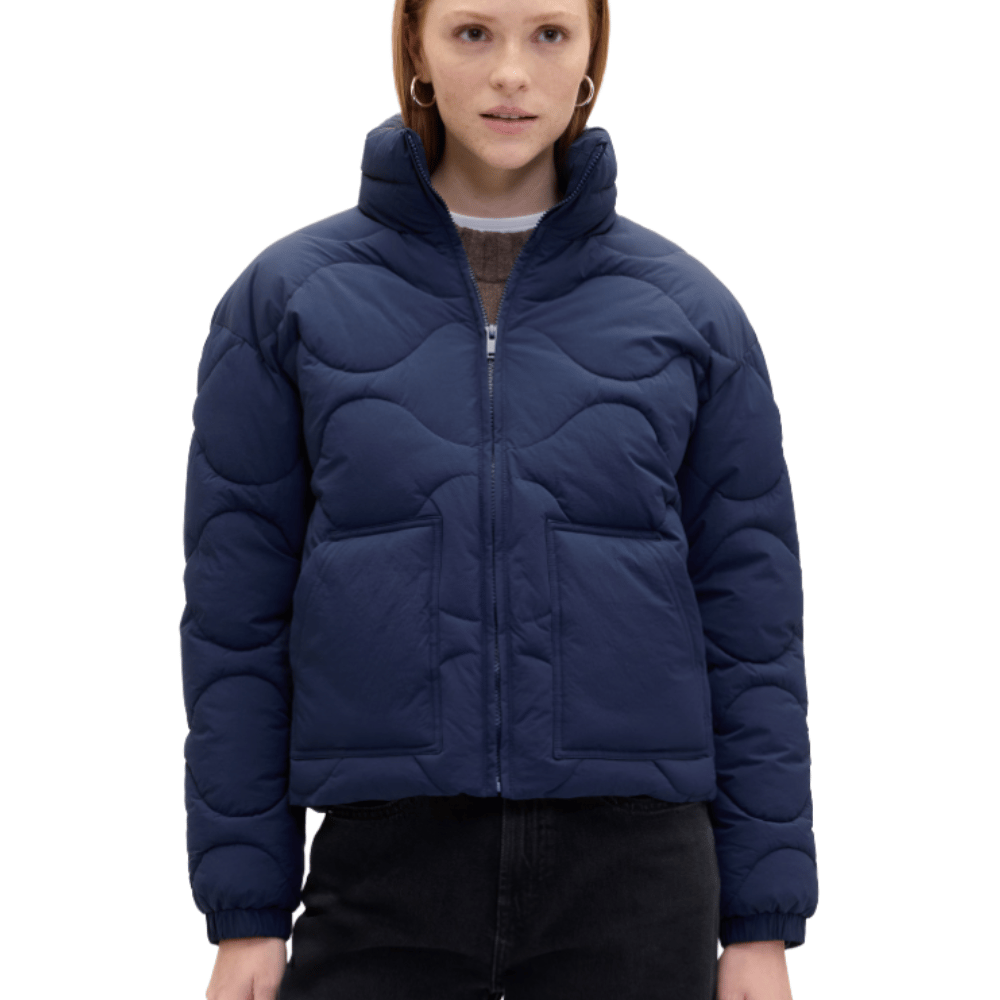 A person wearing a navy blue quilted jacket with a wavy pattern, high collar, side pockets, and a front zipper, paired with black pants.