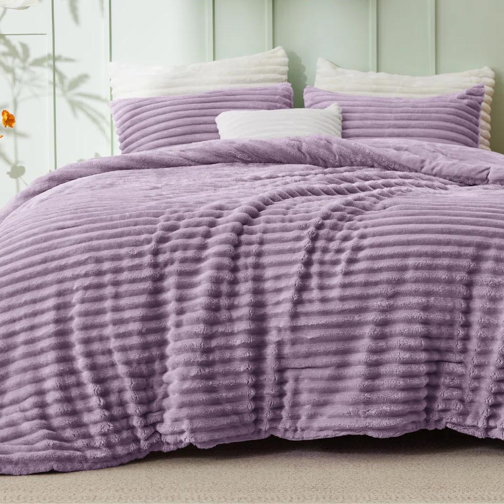 A plush, lavender-colored quilt set featuring a textured, ribbed pattern, paired with matching pillowcases and a white accent pillow.