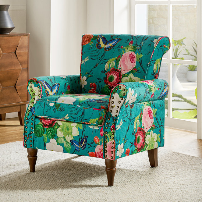 A colorful floral and butterfly patterned armchair with nailhead accents on arms and wooden legs.