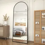 Full-length arched floor mirror with a black frame, flanked by a wooden sideboard and a bookshelf.