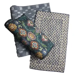 Three folded rugs with different designs: a blue geometric pattern, a beige and blue textured pattern, and a rolled-up floral pattern with multicolored flowers on a dark background.