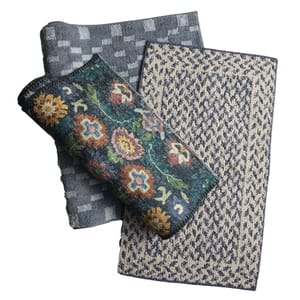 Three folded rugs with different designs: a blue geometric pattern, a beige and blue textured pattern, and a rolled-up floral pattern with multicolored flowers on a dark background.