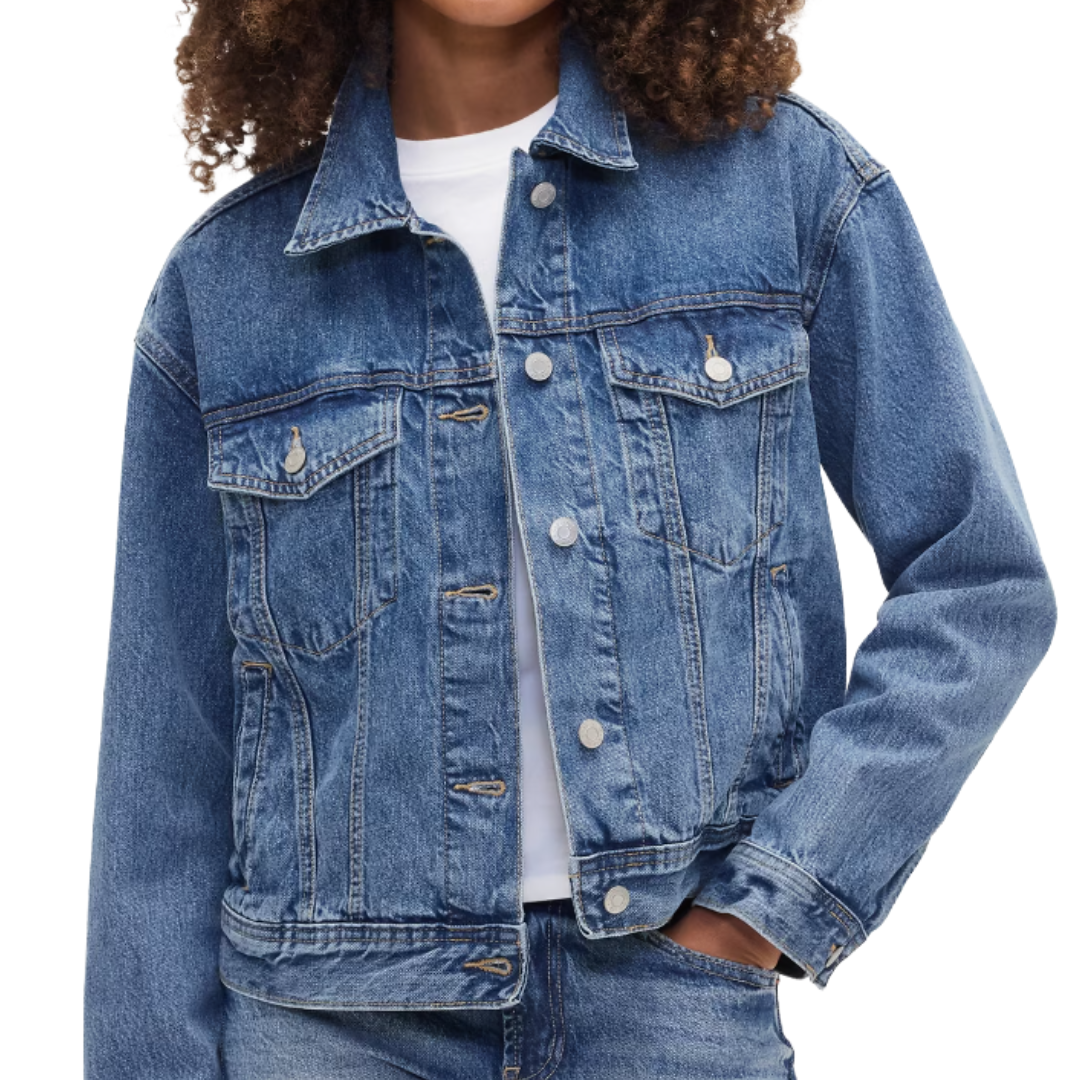 A person is wearing a classic denim jacket with a front button closure and chest pockets over a white shirt, paired with blue jeans.